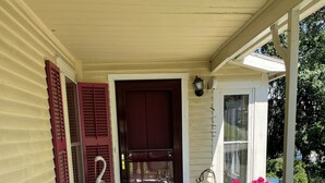 A porch with a white metal chair, a dark door, and a small garden area with flowers.