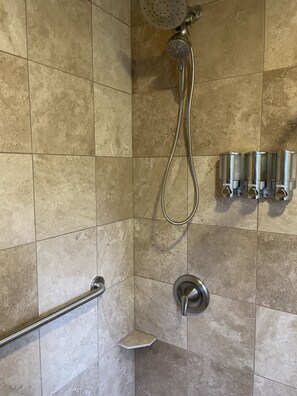Shower area features a handheld showerhead, wall-mounted showerhead, and grab bar for added safety.