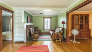 A spacious living room with hardwood floors, a fireplace, a sofa, a rocking chair, and a fan.