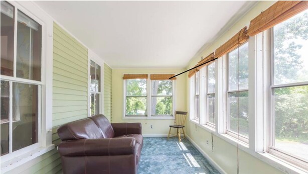 A room with a brown leather sofa, a wooden chair, and large windows with white frames.