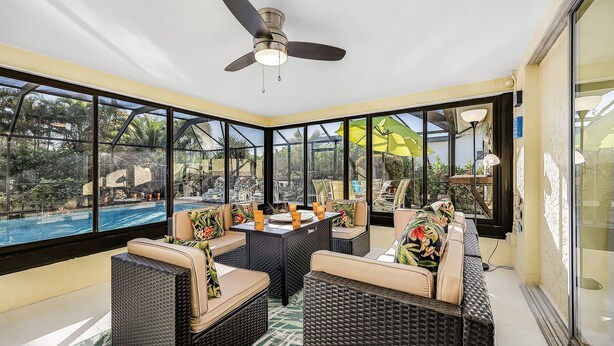 A sunroom with wicker furniture, a ceiling fan, and a view of a swimming pool.