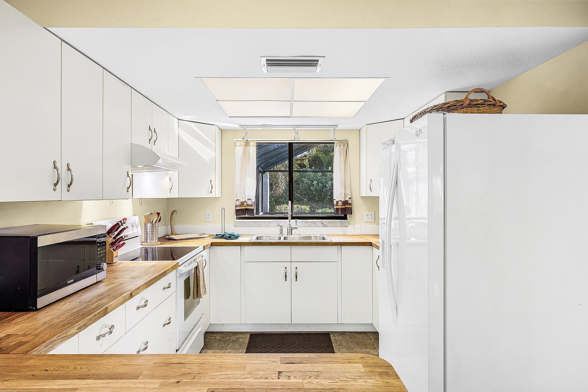 A kitchen with white cabinets, a microwave, a sink, and a window with curtains.