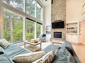 Een moderne woonkamer met een stenen openhaard, grote ramen en een boekenplank.