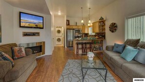 A spacious living area with a fireplace, a television mounted on the wall, and a kitchen with wooden cabinets and a central island.