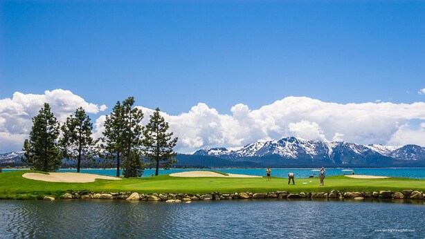 A golf course with a lake, mountains, and trees.