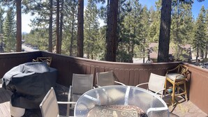 A deck with a covered grill, outdoor seating, and a view of a forested area.