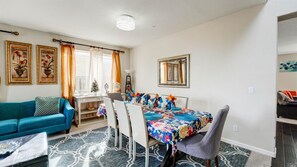 A living room with a blue sofa, a dining table with a floral tablecloth, and a chandelier. - MODERN NEWER HOME CLOSE TO NAPA WINE COUNTRY, SACRAMENTO &  SAN FRANCISCO (FAIRFIELD)