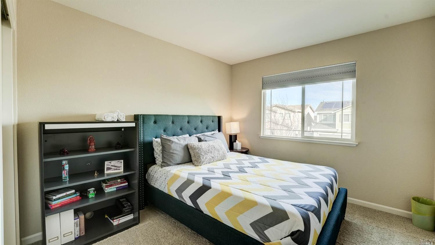 Une chambre à coucher avec un lit, une bibliothèque, une fenêtre et une vue sur les bâtiments à l’extérieur.