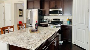 A kitchen with dark wooden cabinets, stainless steel appliances, a granite countertop, and a dining area with chairs. - MODERN NEWER HOME CLOSE TO NAPA WINE COUNTRY, SACRAMENTO &  SAN FRANCISCO (FAIRFIELD)