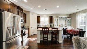 A modern kitchen with stainless steel appliances, a central island with bar stools, and a dining area with a table and chairs. - MODERN NEWER HOME CLOSE TO NAPA WINE COUNTRY, SACRAMENTO &  SAN FRANCISCO (FAIRFIELD)