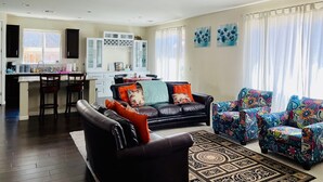 A living room with a black leather sofa, colorful patterned chairs, a dining area with a white cabinet, and a kitchen with a window. - MODERN NEWER HOME CLOSE TO NAPA WINE COUNTRY, SACRAMENTO &  SAN FRANCISCO (FAIRFIELD)