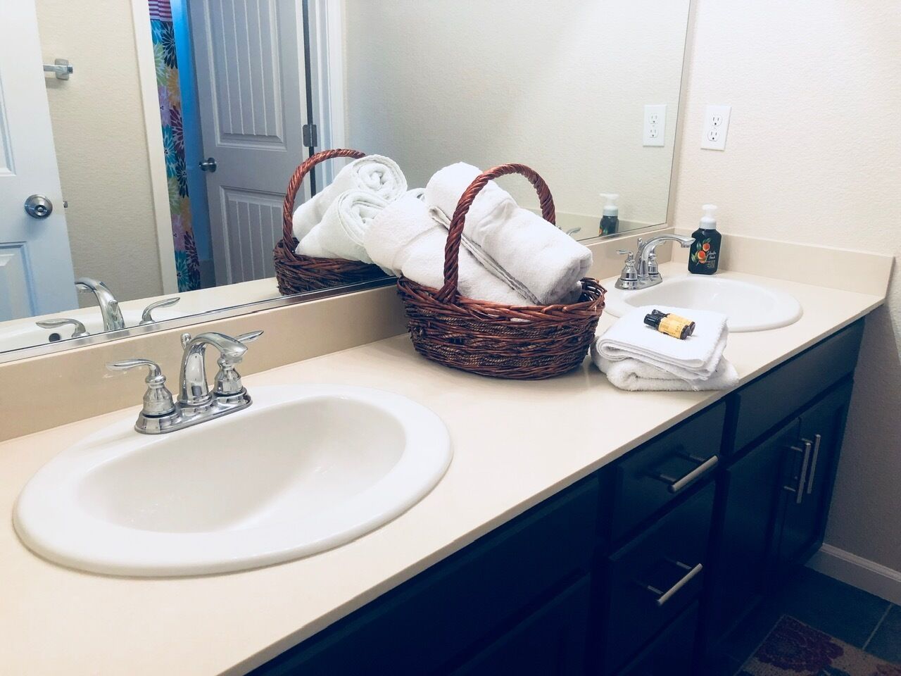 A bathroom with a white sink, a mirror, a wicker basket with towels, and a bottle of hand soap.