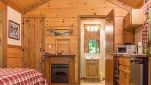 Een gezellig chalet met een open haard, een kitchenette met een magnetron, en een bed met een ruitdessin deken.