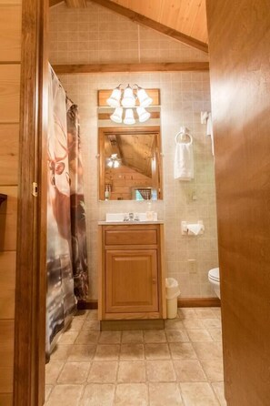 A bathroom with wooden cabinets, a tiled floor, a sink, a mirror, and a shower curtain.