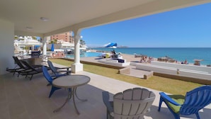 Área externa coberta com cadeiras de descanso, piscina e vista para o mar.