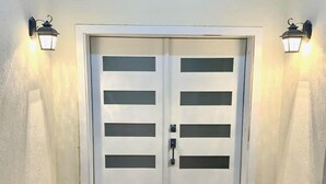 Uma porta dupla com design moderno, ladeada por dois apliques na parede.
