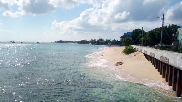 A beach with clear water, a sandy shore, and a concrete walkway.