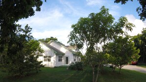 A white house with a green roof, surrounded by trees and a lawn.