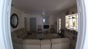 A living room with a sectional sofa, a coffee table, two chairs, a TV, and a bookshelf.