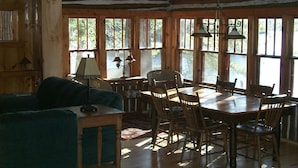 A rustic cabin interior with a dining table, chairs, a sofa, and a lamp.