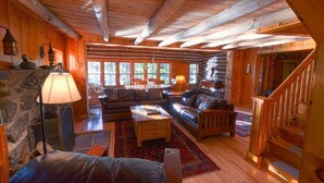 A log cabin interior with a fireplace, leather furniture, and a wooden staircase.