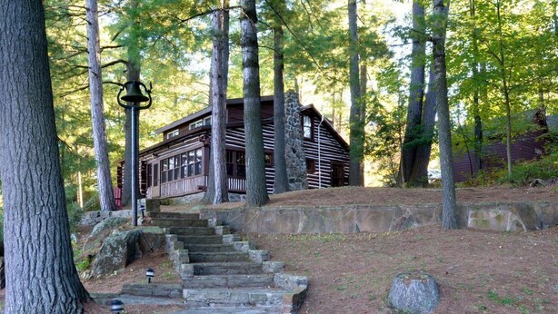 A rustic cabin with a stone staircase leading up to it, surrounded by tall trees.