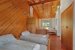 Uma cabana com duas camas, um ventilador de teto e uma janela com cortinas.