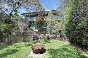 Uma casa com varanda coberta, lareira e escadas que levam a um andar superior com telhado verde.