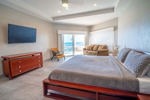 Quarto com uma cama grande, cômoda de madeira, cadeira e televisão na parede.