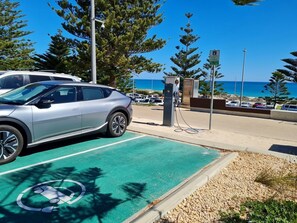 A parking area with electric vehicle charging stations, a clear view of the ocean, and a parking lot with cars. - The Sea Breeze Penthouse Apartment (Scarborough)