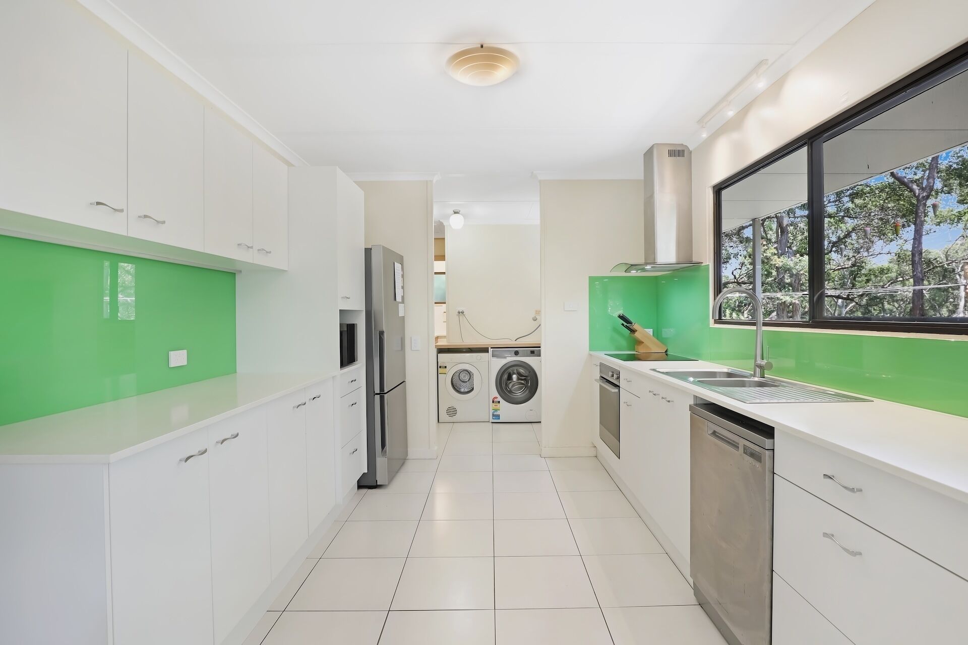 A modern kitchen with white cabinets, a stainless steel refrigerator, a washing machine, and a dishwasher.