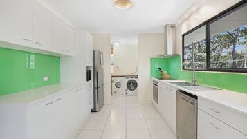 A modern kitchen with white cabinets, a stainless steel refrigerator, a washing machine, and a dishwasher.