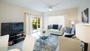 Ein modernes Wohnzimmer mit Flachbildfernseher, einer Couch, einem Couchtisch und einem Deckenventilator.