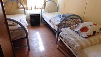 A small, compact room with two metal bunk beds, a small bedside table, and a window with curtains.