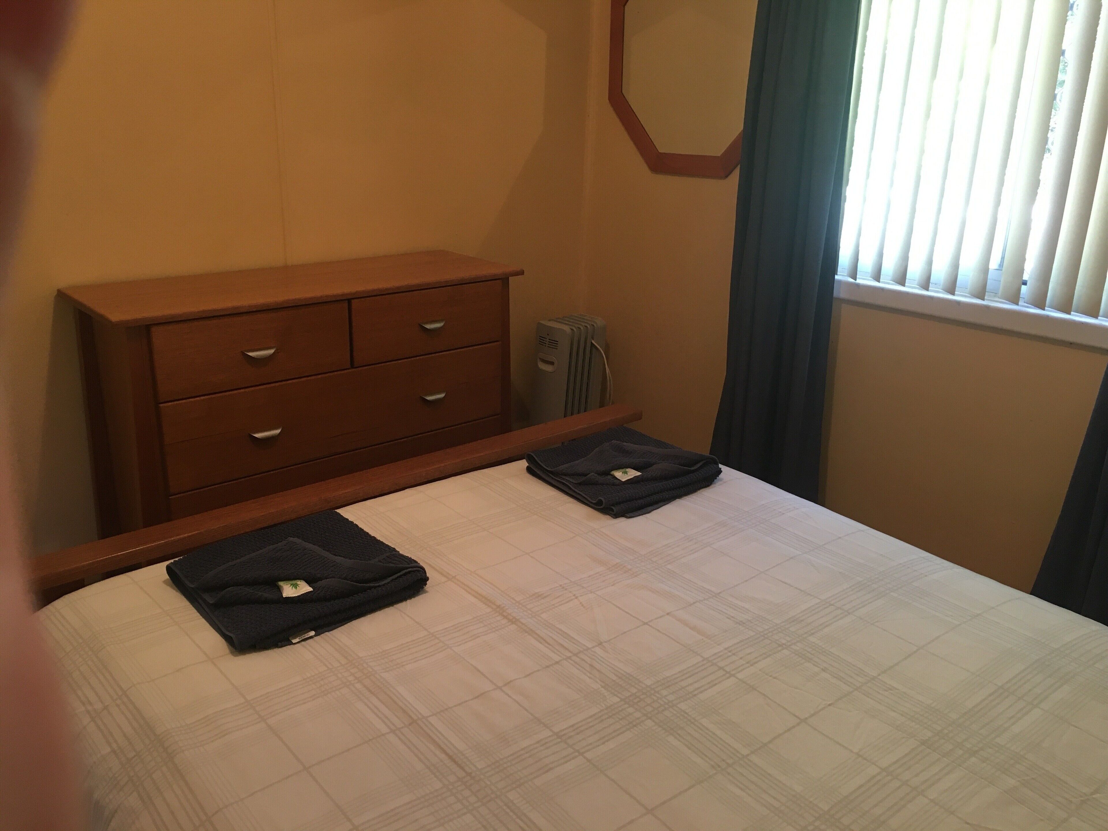 A hotel room with a bed, a wooden dresser, and a radiator.