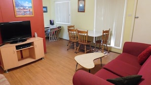 A living room with a TV, red sofa, wooden dining table, and chairs.