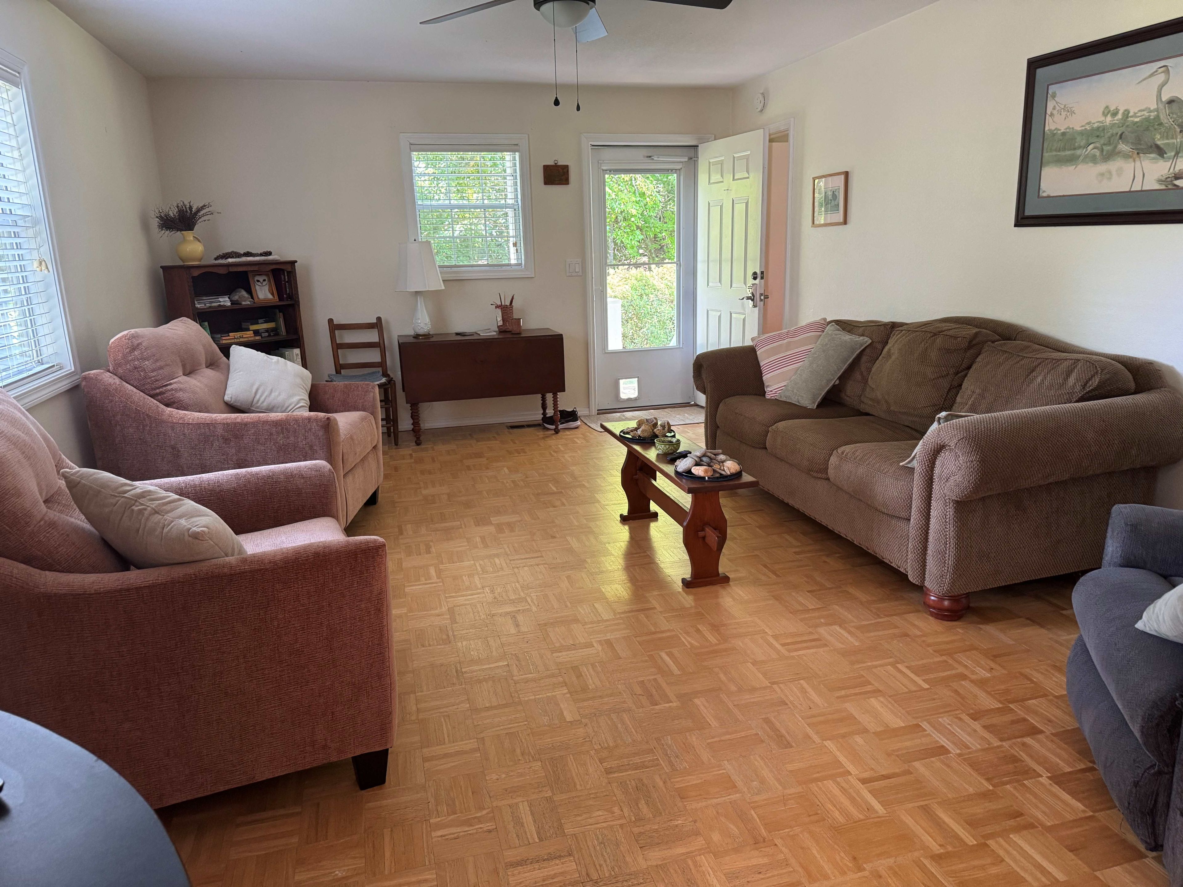 A living room with a brown sofa, two armchairs, a wooden coffee table, and a bookshelf.
