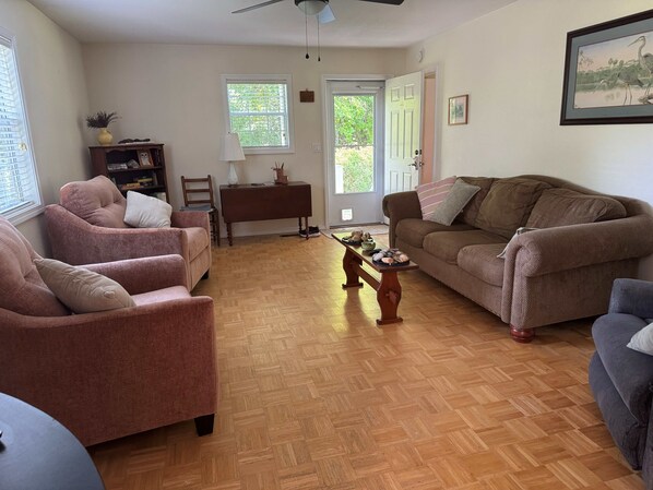 A living room with a brown sofa, two armchairs, a wooden coffee table, and a bookshelf.