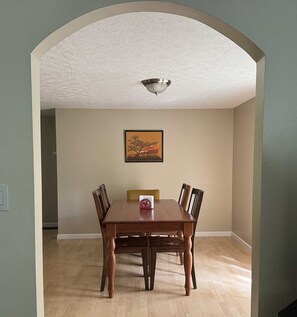 Een eethoek met een houten tafel en stoelen, een schilderij aan de muur en een plafondlamp.