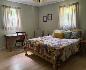 A bedroom with a bed, a desk, a chair, and two windows with curtains.
