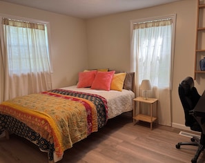 Une chambre à coucher avec un lit, une table de chevet, une lampe, une chaise et des rideaux.