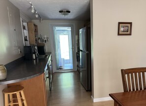 A kitchen with a refrigerator, stove, and a coffee maker. There is a wooden chair and a stool.