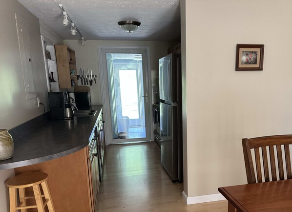 A kitchen with a refrigerator, stove, and a coffee maker. There is a wooden chair and a stool.