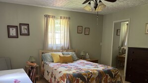 Une chambre à coucher comprenant un lit, un bureau, une chaise, une commode et un ventilateur de plafond.