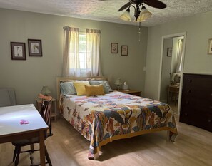 Een slaapkamer met een bed, een bureau, een stoel, een dressoir en een plafondventilator.
