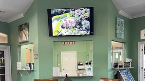 A dining area with a round wooden table, four chairs, a television mounted on the wall, and a small kiosk with magazines. - Your perfect stay starts here. Near Disney/Universal. (Kissimmee)