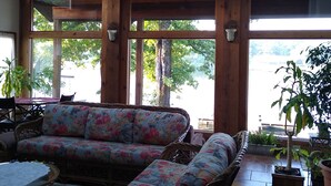A spacious room with wooden beams, large windows, a ceiling fan, and a floral sofa. - Anderson Lake House  (Hot Springs)