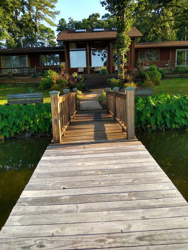A wooden pier leading to a building with a covered porch and large windows.