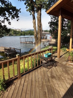 A wooden deck with a railing overlooking a lake, dock, and a gazebo.