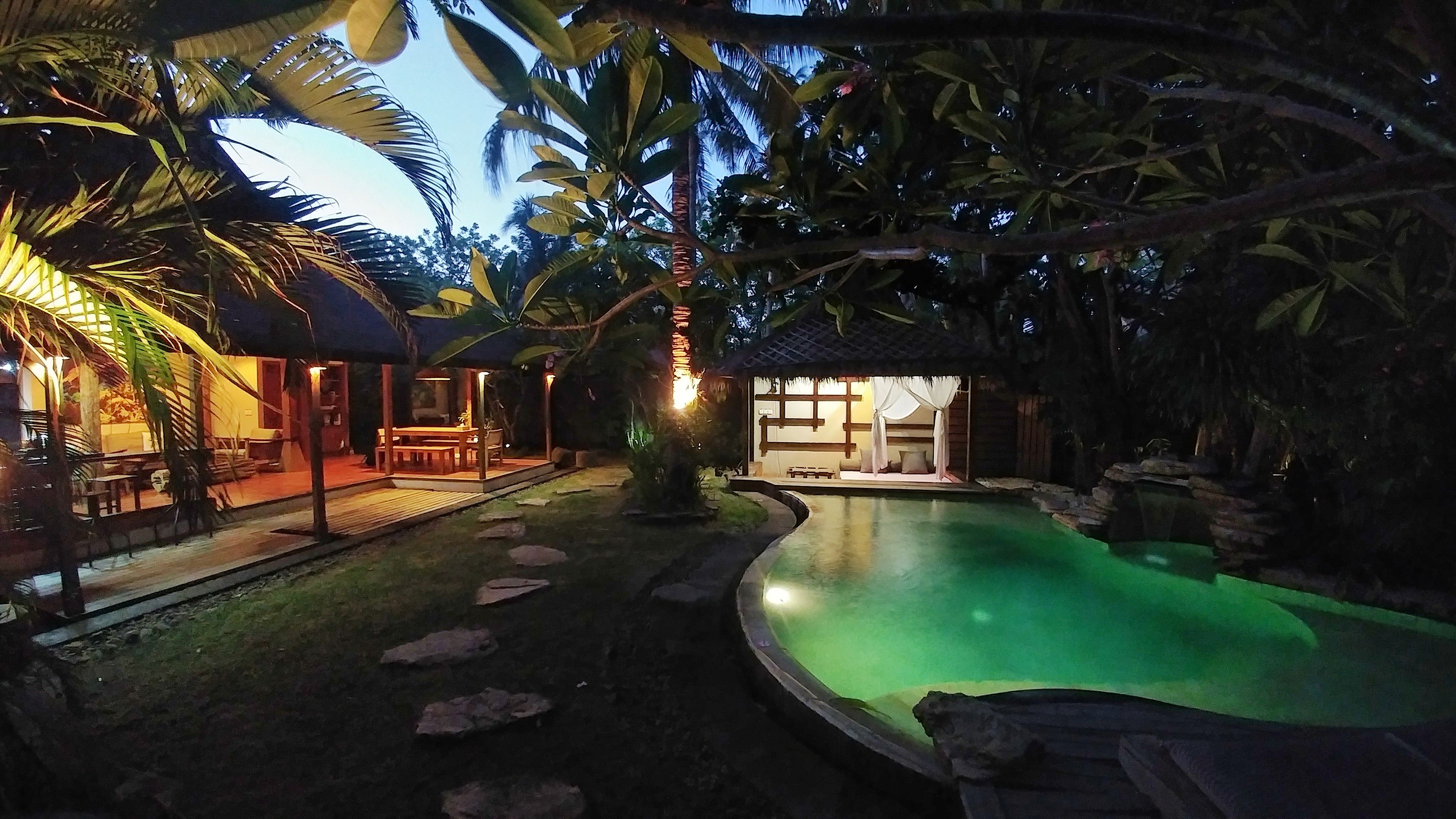 A poolside area with a thatched-roof structure, a dining area, and a lounge with a view of the pool.